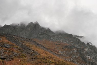 Mystical background with dramatic mountains. Rain in mountains. Atmospheric misty landscape with fuzzy silhouettes of sharp rocks in low clouds during rain. 