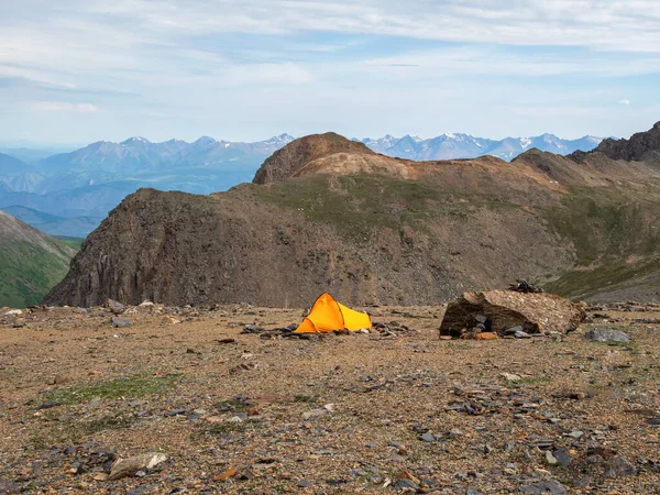 Summer camping in mountain. Bright alpine landscape with vivid orange tent at very high altitude with view to high mountain and large glacier in dramatic clouds. Awesome mountain scenery with tent.