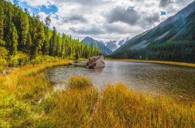 Gölün ortasında büyük bir granit taş var. Highland Valley 'de yüksek dağ boyunca güzel bir göl. Dağ gölünün taşlı durgun suları. Dağlık arazilerin sarı atmosferik doğal arkaplanı.