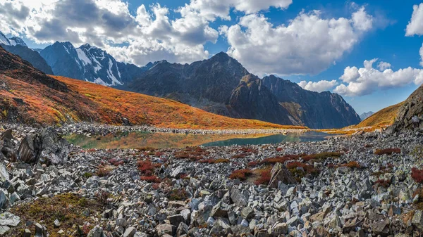 Panoramic view of the autumn mountain lake with reflection white clouds. A clear blue mountain lake and a bright autumn stones floating in water.