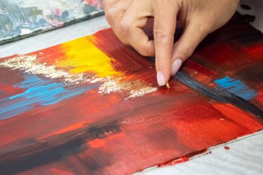 Selective focus. Female hands apply gold potal to the picture. Potal painting technique, applying gold leaf particles to an interior painting.