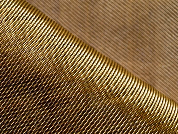 Selective focus. The bend of the golden fabric bulletproof material aramid. Aramid kevlar background. Golden kevlar texture and pattern. Copy space.
