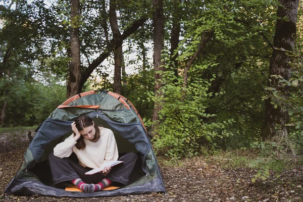 Una giovane donna dentro una tenda nel bosco. Leggere un libro in natura. Comodo riposo in natura — Foto Stock