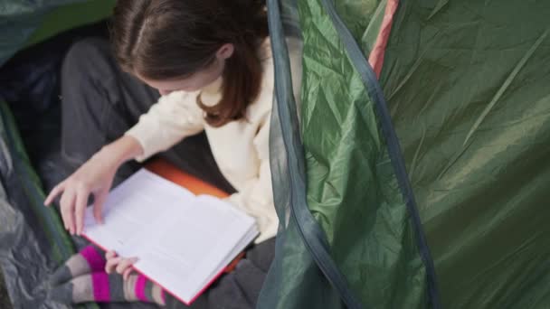 Leyendo un libro en una tienda. Vacaciones relajantes en la naturaleza. Una joven descansa en un campamento — Vídeo de stock