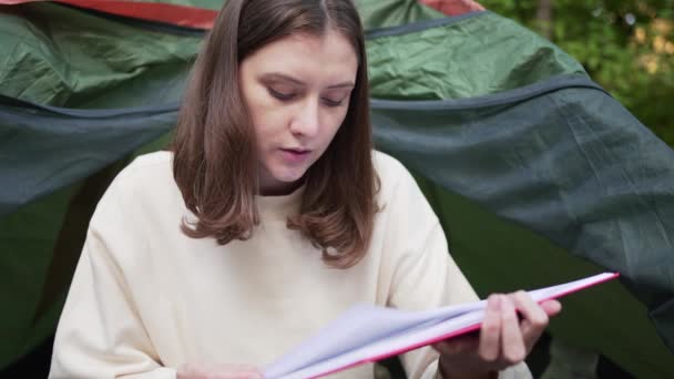 Rilassati nel campo. Una bella giovane donna legge un libro in una tenda individuale. Foresta, riposo attivo — Video Stock