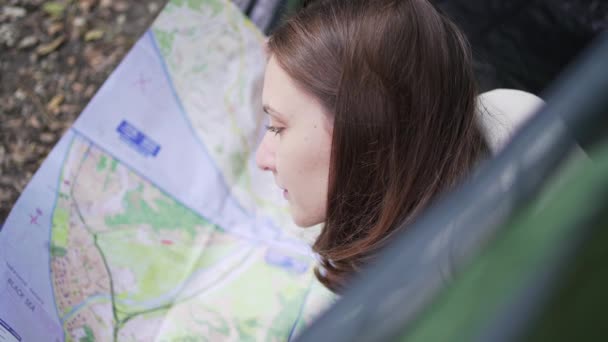 Una mujer viajera estudia el mapa mientras está acostada en una tienda. Abre una nueva dirección para la caminata. Turista de trekking — Vídeos de Stock