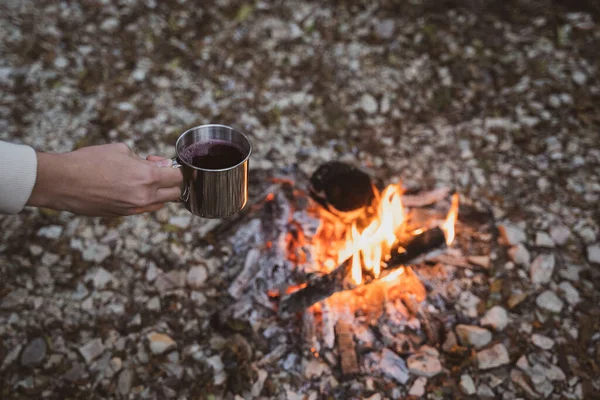 Cucinare su un fuoco aperto nella foresta. La persona tiene una tazza di metallo sul fuoco e riscalda la bevanda — Foto Stock