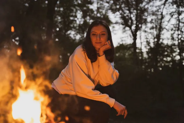 Kampta ateşin yanında genç bir kadın oturuyor. Sıcak ve samimi kamp ateşi