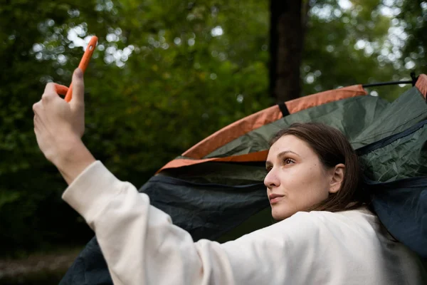 Não há ligação na natureza. Uma mulher tenta entrar em contato por telefone em uma tenda na floresta. Descontente Imagens Royalty-Free