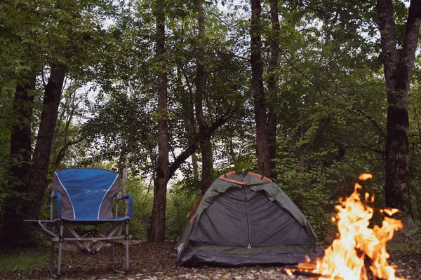 Acampar na floresta. Uma pequena tenda, uma cadeira dobrável e uma fogueira na natureza. Não há pessoas Fotos De Bancos De Imagens Sem Royalties
