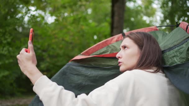 Keine Verbindung in der Natur. Eine Frau versucht, in einem Zelt im Wald telefonisch Kontakt aufzunehmen. Unzufrieden — Stockvideo