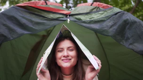 Beautiful young woman fooling around with a map in a tent — Stockvideo