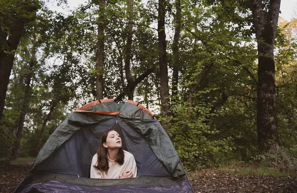 Uma mulher bonita olha para fora da tenda e olha em volta na floresta. Retrato de um turista em uma caminhada Fotografias De Stock Royalty-Free