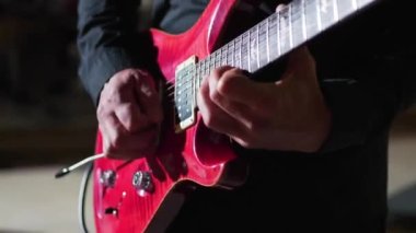 Gitarist bir enstrüman çalıyor. Gösteride kırmızı gitar, yakın plan.