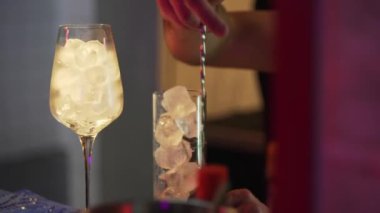 Gece barı. Yakın plan - barmen kokteyl için buzu uzun kaşıkla karıştırıyor. Bir bardak alkol.