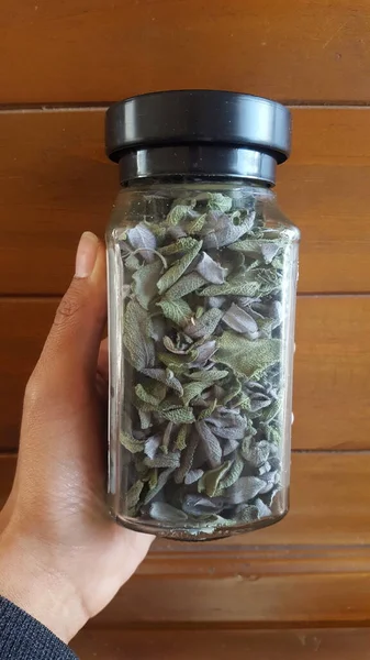 Ahşap arka planda cam bir kavanozda kurumuş yeşil yapraklar.
