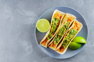 Meksika yemeği. Gri tabakta kızarmış et ve guacamole soslu taco. Gri arka planda Meksika tacoları ve limon dilimleri. Uzayı kopyala Üst görünüm