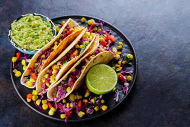 Tatlı mısır, mor lahana ve siyah tabakta domatesli vejetaryen tacoları. Sebzeli taco ve arka planda guacamole sosu. Uzayı kopyala Üst görünüm