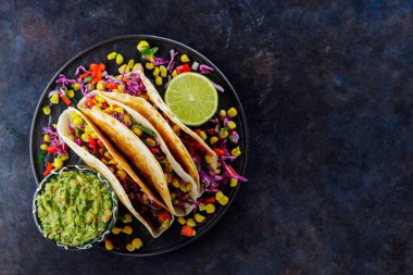 Tatlı mısır, mor lahana ve siyah tabakta domatesli vejetaryen tacoları. Sebzeli taco ve arka planda guacamole sosu. Uzayı kopyala Üst görünüm