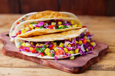 Kesme tahtasında çeşitli sebzelerle vejetaryen tacoları. Tatlı mısırlı tacolar, mor lahana ve tahta tahtada domatesler. Boşluğu kopyala