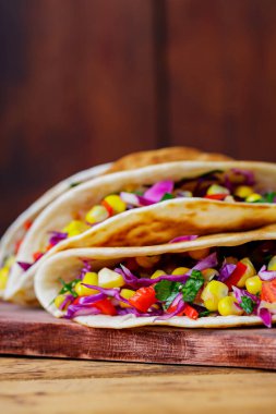 Kesme tahtasında çeşitli sebzelerle vejetaryen tacoları. Tatlı mısırlı tacolar, mor lahana ve tahta tahtada domatesler. Boşluğu kopyala