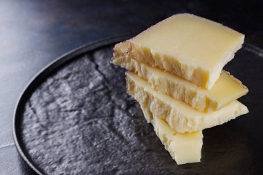 Koyu arkaplanda sert peynir parçaları. Tahtada keçi peyniri. Uzun zamandır olgunlaşmış zanaat peyniri. Boşluğu kopyala