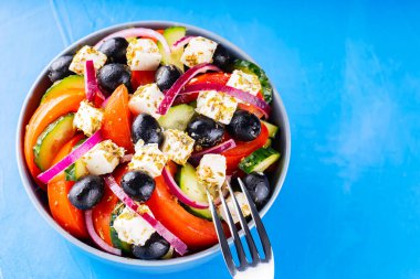 Mavi arka planda Yunan salatası ve çatal. Taze sebze, peynir ve siyah zeytin. Moda yemekler. Uzayı kopyala Üst görünüm