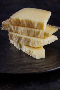 Koyu arkaplanda sert peynir parçaları. Tahtada keçi peyniri. Uzun zamandır olgunlaşmış zanaat peyniri. Boşluğu kopyala