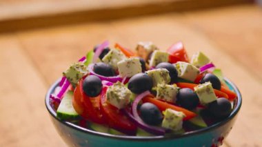 Yunan salata hazırlama süreci. Zeytinyağı, limon suyu ve kekik otu karışımı Yunan salatasına dökülür. Sağlıklı gıda konsepti. Yakın plan.