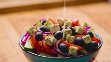 Yunan salata hazırlama süreci. Zeytinyağı, limon suyu ve kekik otu karışımı Yunan salatasına dökülür. Sağlıklı gıda konsepti. Yakın plan.