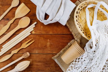 Ahşap mutfak gereçleri ve tahta masada ip torbası. Tahta çatal bıçaklar eski tahtalarda. Tek kullanımlık kağıt bardaklar ve keten poşetler. Sıfır atık. Üst görünüm