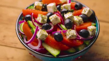 Tahta bir kasede Yunan salatası. Kamera Yunan salatasının üzerinde hareket ediyor. Sebzeli, peynirli ve zeytinli yaz salatası. Elle ateş