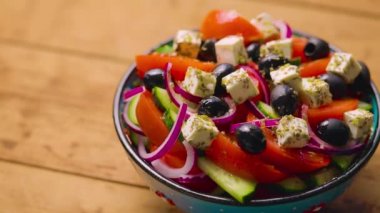 Tahta bir kasede Yunan salatası. Kamera Yunan salatasının üzerinde hareket ediyor. Sebzeli, peynirli ve zeytinli yaz salatası. Elle ateş