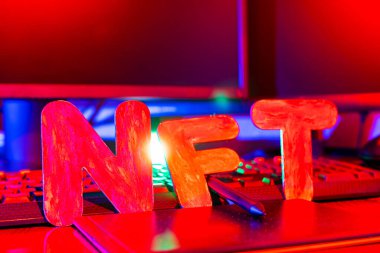 Neon ışığıyla aydınlatılmış harflerin NFT (Parasız Token) metni. NFT dijital sanat yaratan bir grafik tasarımcısının işyeri. Kriptoart ve engelleme teknolojisi kavramı