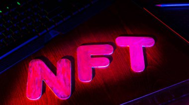 Neon ışığıyla aydınlatılmış harflerin NFT (Parasız Token) metni. NFT dijital sanat yaratan bir grafik tasarımcısının işyeri. Kriptoart ve engelleme teknolojisi kavramı