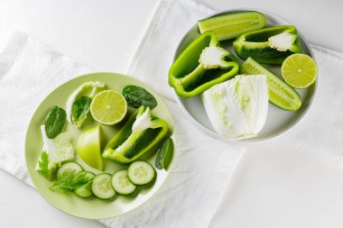 Dilimlenmiş yeşil sebze ve tabakta meyveler. Beyaz arka planda yeşil diyet yemeği. Sağlıklı ve vejetaryen yemekleri. Üst görünüm