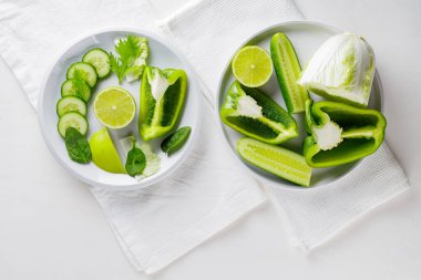 Dilimlenmiş yeşil sebze ve tabakta meyveler. Beyaz arka planda yeşil diyet yemeği. Sağlıklı ve vejetaryen yemekleri. Üst görünüm