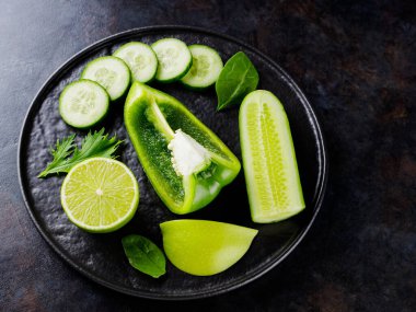 Koyu bir arka planda yeşil sebzeler ve meyveler. Siyah tabakta yeşil diyet yemeği. Sağlıklı yiyecekler. Üst Manzara. Boşluğu kopyala