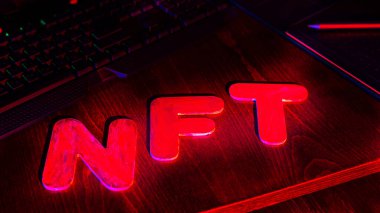 Neon ışığıyla aydınlatılmış harflerin NFT (Parasız Token) metni. NFT dijital sanat yaratan bir grafik tasarımcısının işyeri. Kriptoart ve engelleme teknolojisi kavramı