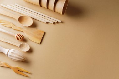 Bej arka planda çevre dostu ahşap çatal bıçak seti. Plastiksiz konsept. Tek kullanımlık kağıt bardaklar ve ahşap mutfak gereçleri. Sıfır atık