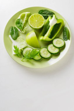 Yeşil bir tabakta doğranmış yeşil meyve ve sebzeler. Beyaz arka planda taze yeşil diyet yiyecekler. Sağlıklı vejetaryen gıda konsepti. Uzayı kopyala Üst görünüm