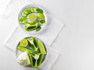 Dilimlenmiş yeşil sebze ve tabakta meyveler. Beyaz arka planda yeşil diyet yemeği. Sağlıklı ve vejetaryen yemekleri. Üst görünüm