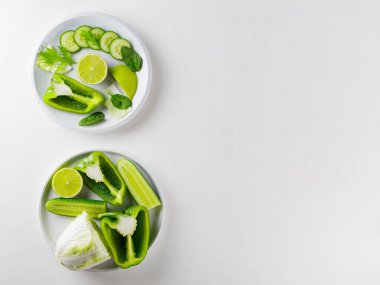 Beyaz arka planda doğranmış yeşil sebzeler ve meyveler. Beyaz tabakta yeşil diyet yemeği. Sağlıklı ve vejetaryen yemekleri. Üst Manzara. Boşluğu kopyala