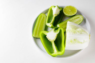 Beyaz arka planda doğranmış yeşil sebzeler ve meyveler. Beyaz tabakta yeşil diyet yemeği. Sağlıklı ve vejetaryen yemekleri. Üst Manzara. Boşluğu kopyala