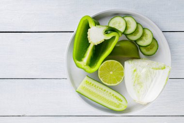 Beyaz bir tabakta dilimlenmiş yeşil meyve ve sebzeler. Beyaz tahtalarda yeşil diyet yiyecekler. Sağlıklı ve vejetaryen yemekleri. Üst Manzara. Boşluğu kopyala