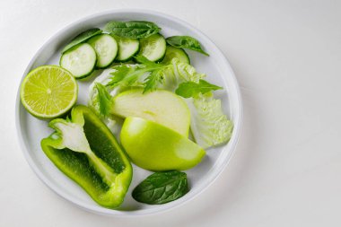 Beyaz bir tabakta dilimlenmiş yeşil meyve ve sebzeler. Beyaz arka planda taze yeşil diyet yiyecekler. Sağlıklı vejetaryen gıda konsepti. Uzayı kopyala Üst görünüm