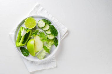 Dilimlenmiş yeşil sebzeler ve beyaz tabakta meyveler. Beyaz arka planda taze yeşil diyet yiyecekler. Uzayı kopyala Üst görünüm