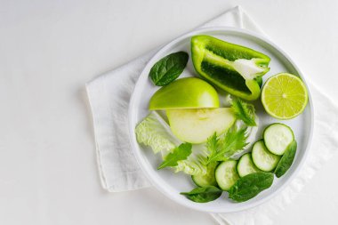 Dilimlenmiş yeşil sebzeler ve beyaz tabakta meyveler. Beyaz arka planda taze yeşil diyet yiyecekler. Uzayı kopyala Üst görünüm