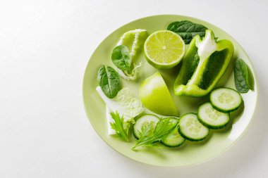 Yeşil bir tabakta doğranmış yeşil meyve ve sebzeler. Beyaz arka planda taze yeşil diyet yiyecekler. Sağlıklı vejetaryen gıda konsepti. Uzayı kopyala Üst görünüm