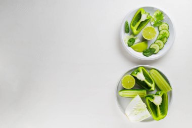 Beyaz arka planda doğranmış yeşil sebzeler ve meyveler. Beyaz tabakta yeşil diyet yemeği. Sağlıklı ve vejetaryen yemekleri. Üst Manzara. Boşluğu kopyala